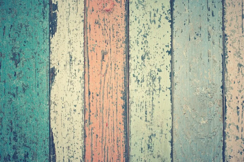 Weathered wooden floorboards with peeling paint in turquoise, cream, coral, and sage green